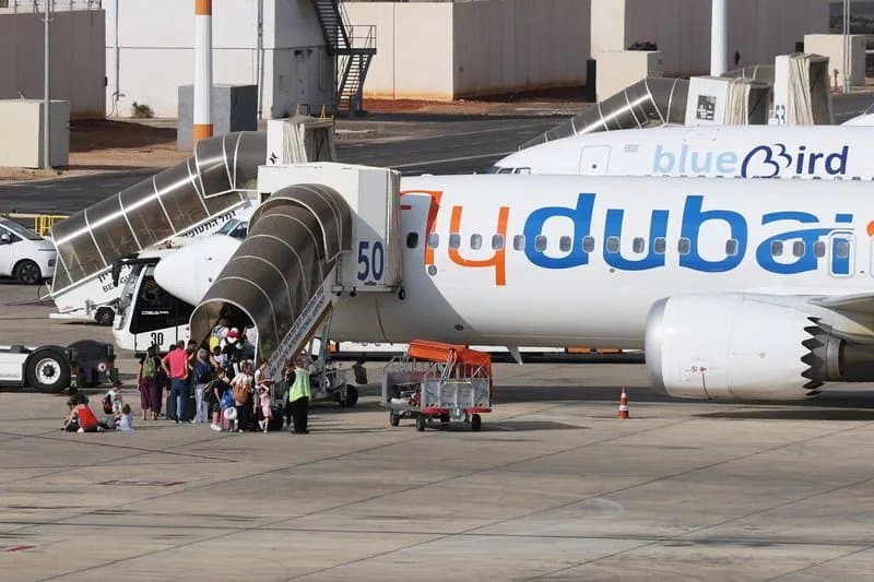 Pasajeros suben por una escalerilla a un avión de flydubai estacionado en la plataforma de un aeropuerto, junto a una aeronave de Blue Bird