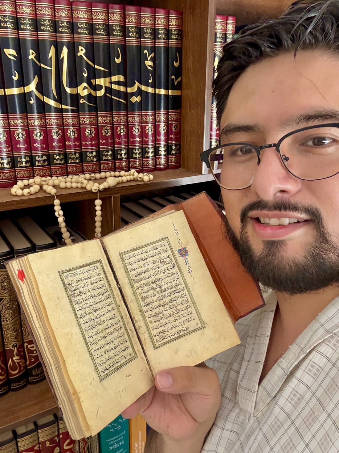 Mullah Khalid sosteniendo un manuscrito antiguo del Corán ante su biblioteca